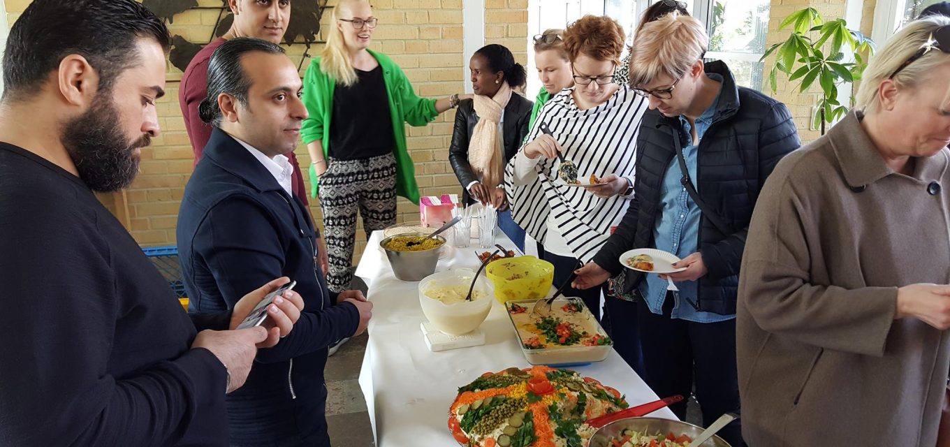 Bild från öppet hus där deltagare från etableringskursen står intill en buffet de förberett och en kö av hungriga besökare