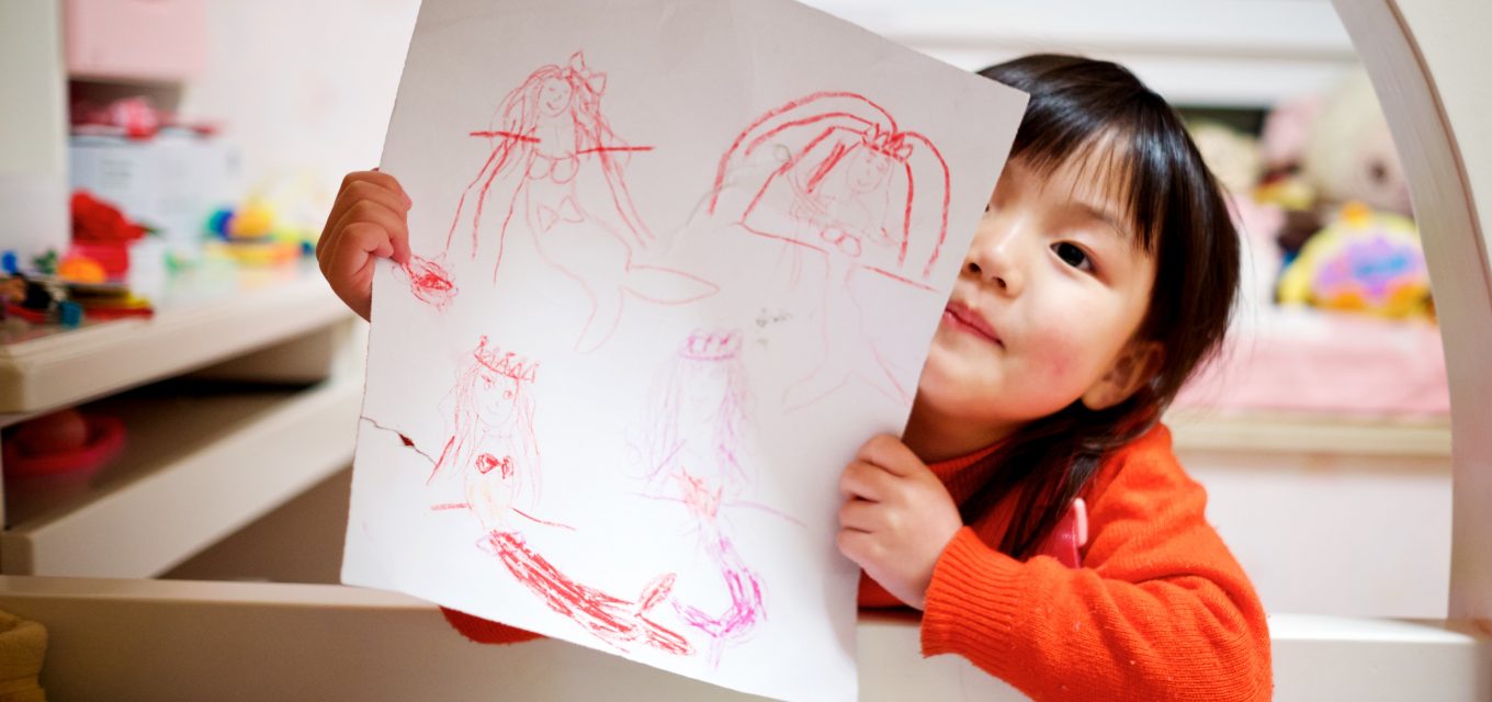 Ett barn håller upp en teckning mot kameran med ett barnrum i bakgrunden