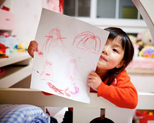 Ett barn håller upp en teckning mot kameran med ett barnrum i bakgrunden