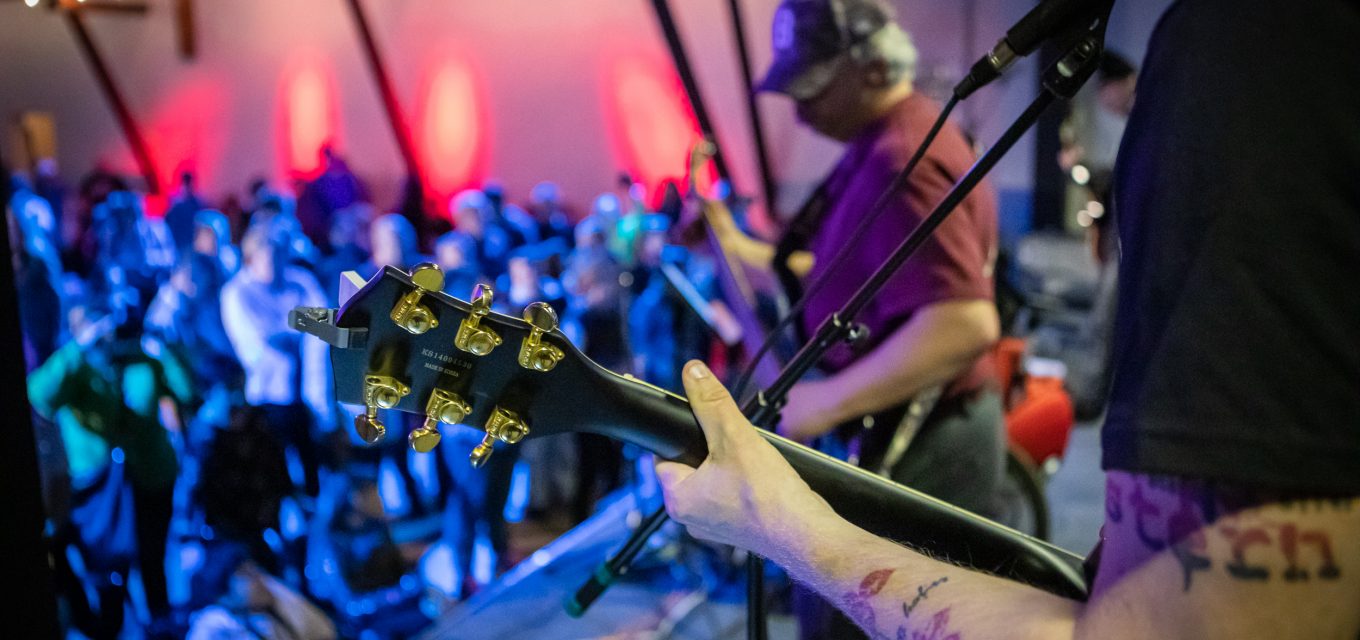 Musiker på scen i förgrund med publik i bakgrunden