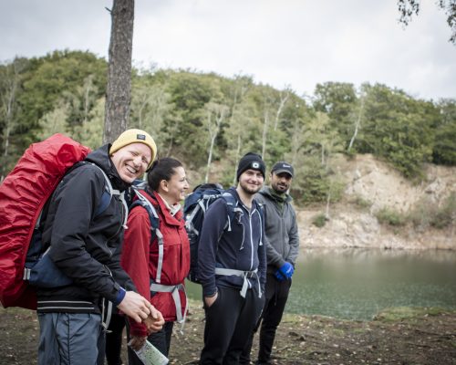 Fyra deltagare fritidsledarutbildningen på naturvandring med ryggsäckar intill en sjö med skog i bakgrunden