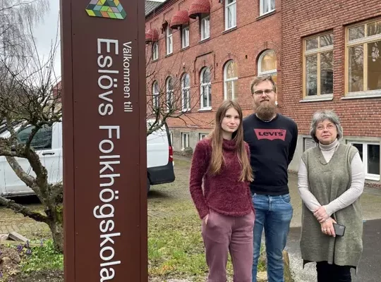 Projektansvarig Care of Folkbildningen och två deltagare i projektet för Ukrainska flyktingar intill en Eslövs folkhögskolas entréskylt