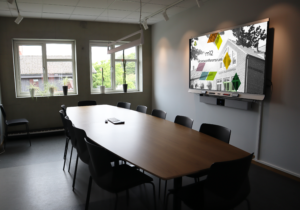 Konferendsum med ett avlångt bord med stolar och en interaktiv skärm på väggen